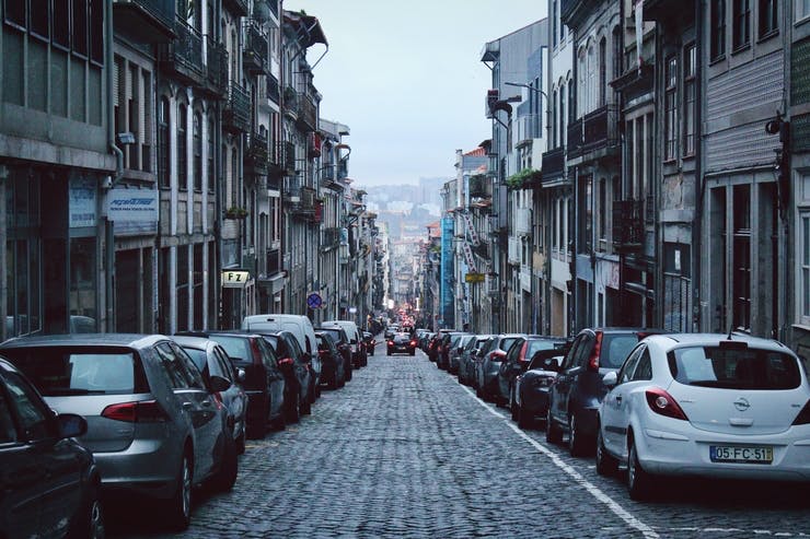 cars parked on each side of a narrow cobblestone street