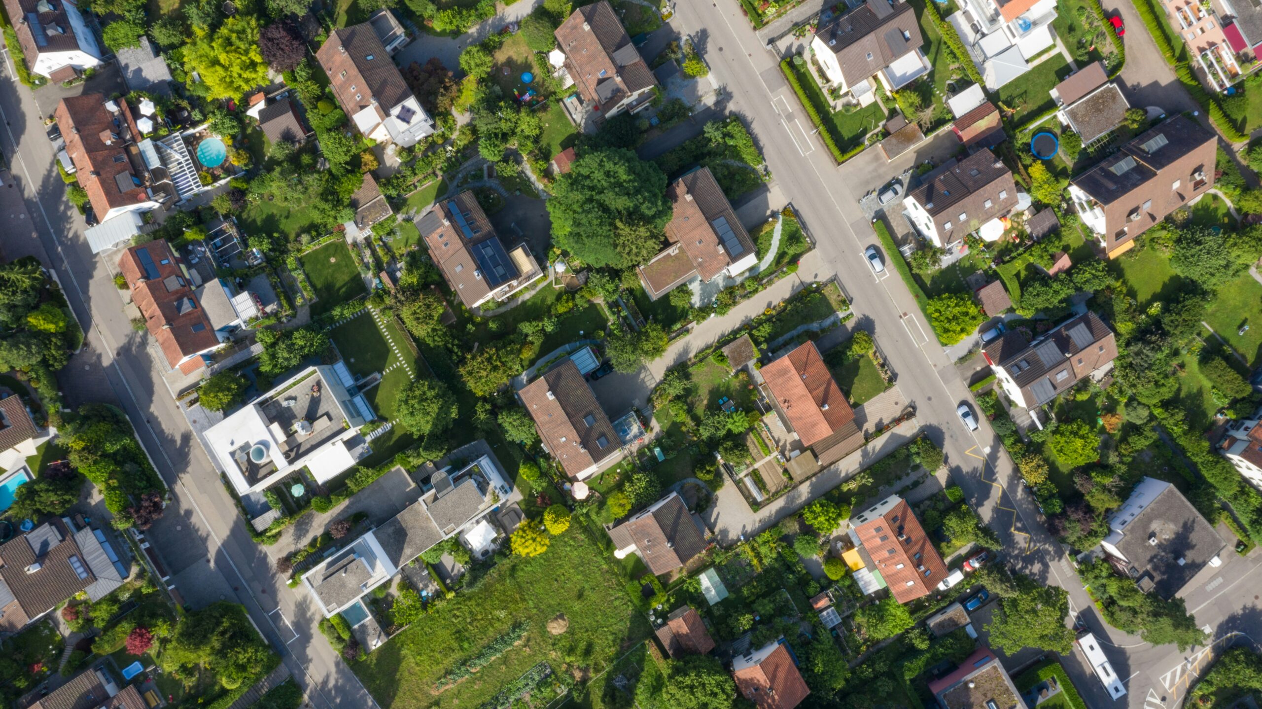 Aerial view of a neighborhood including houses, cars, streets, and greenery