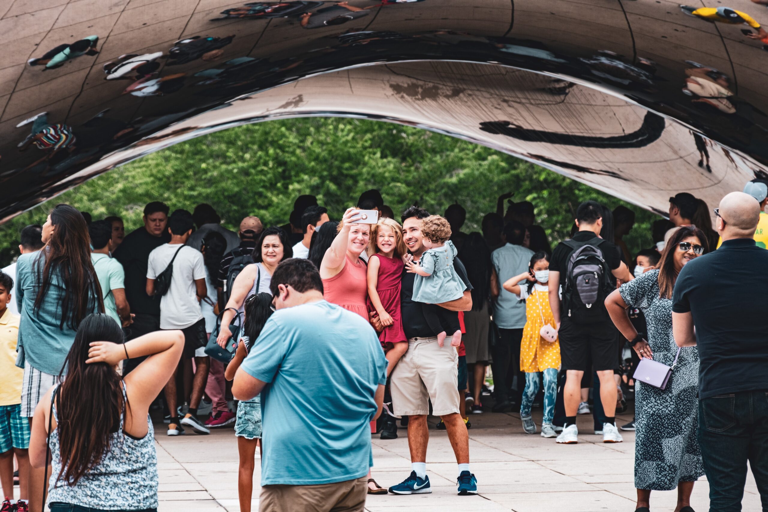 Family composed of a mother, father, and two daughters taking a selfie among the crowd in front of The Bean in Chicago