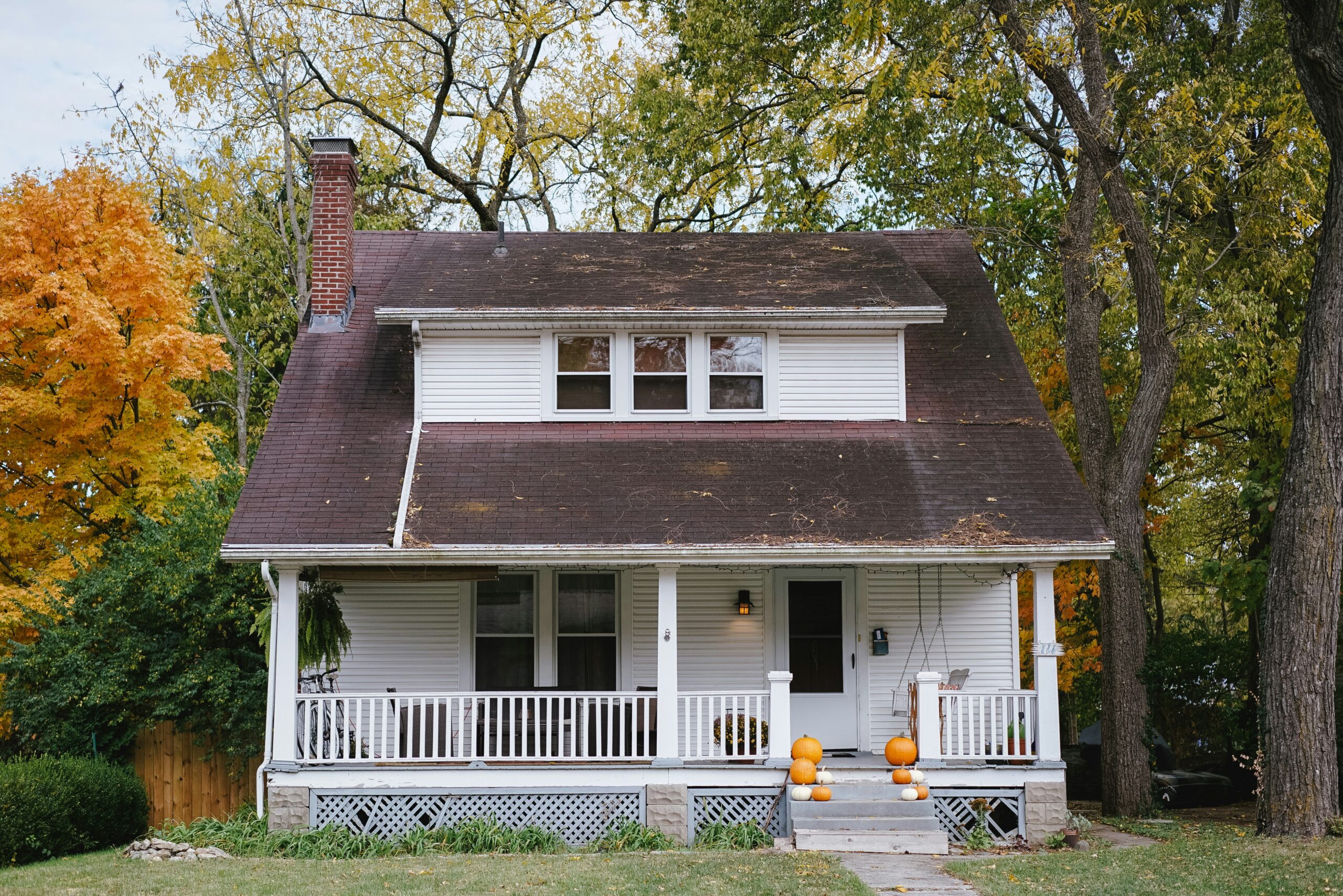 a white house with brown rooftop against a fall backdrop of trees and colorful leaves