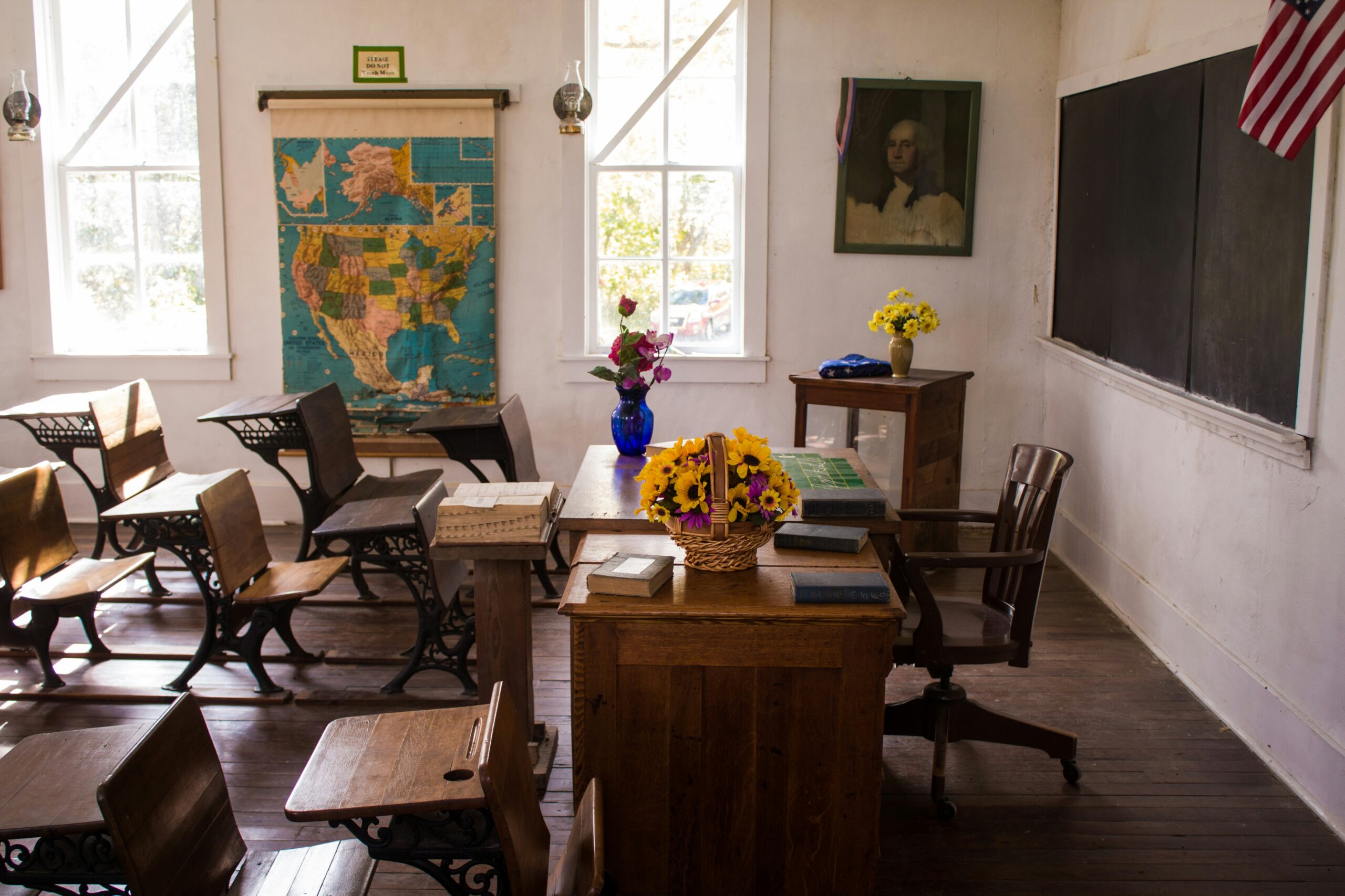 rows of wooden school desk and chairs inside a classroom facing the chalkboard